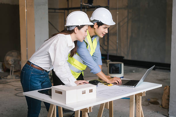 istock Asian male and female engineers wearing safety vests and helmets inspect structural elements, review blueprints, plan material choices bricks, steel, concrete during home renovation project on-site. 2222822314