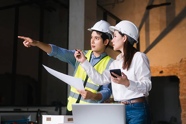 istock Asian male and female engineers wearing safety vests and helmets inspect structural elements, review blueprints, plan material choices bricks, steel, concrete during home renovation project on-site. 2222822333