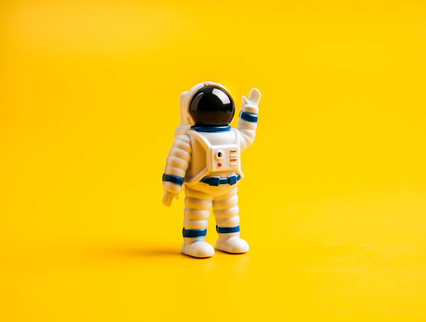 istock Astronaut toy model, standing with raising hand, isolated on yellow background. Plastic tiny astronaut wearing white space suit and helmet, exploration, science and space concept, minimal style. 2222823008