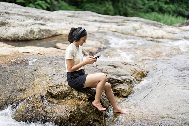 istock Camping and Nature Connection. Woman relaxing by the river while using her smartphone. 2222825360