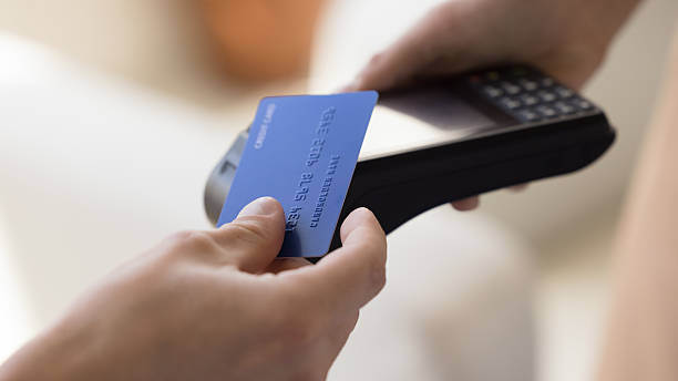 Close up crop view unknown male makes easy, convenient e-payment, holds plastic card against contactless payment terminal equipment, paying for services, food or shopping use wireless NFC technology