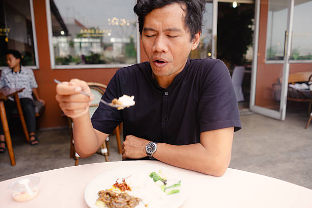 A man is engrossed in enjoying his meal at a restaurant, the focus is on the flavors and the food experience, showing satisfaction and enjoyment. The image captures a moment of culinary pleasure