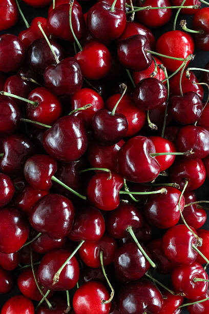 Stock photo shows an overhead full-frame view of fresh red cherries with stems, showcasing their vibrant color and glossy texture. This closeup highlights the juicy ripeness and natural freshness of summer fruit