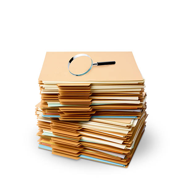 Close-up of magnifying glass on stacked manila folder on white background.