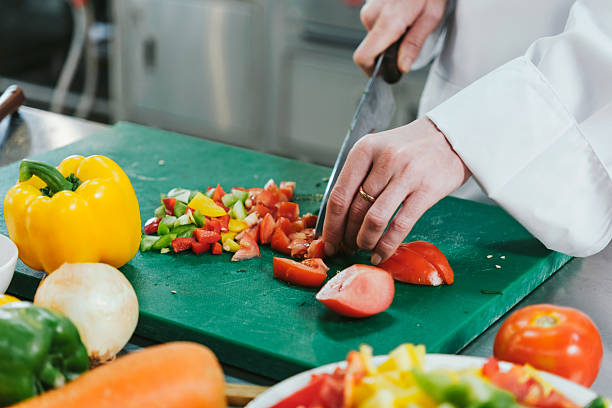 istock Chef in white uniform slicing fresh tomatoes on a green cutting board with chopped bell peppers in a professional kitchen, preparing ingredients for a colorful, healthy dish during cooking class. 2222835135