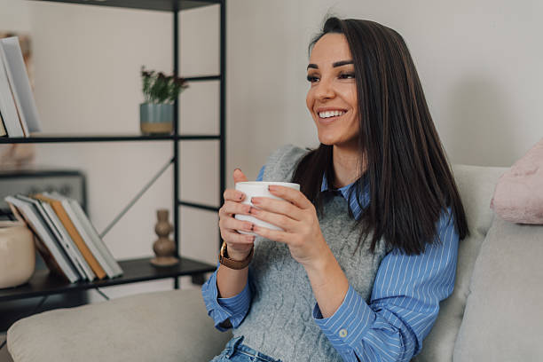istock Smiling woman enjoying hot beverage on sofa at home 2222835430