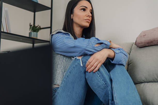istock Sad woman sitting on floor next to sofa and thinking about problems 2222835552