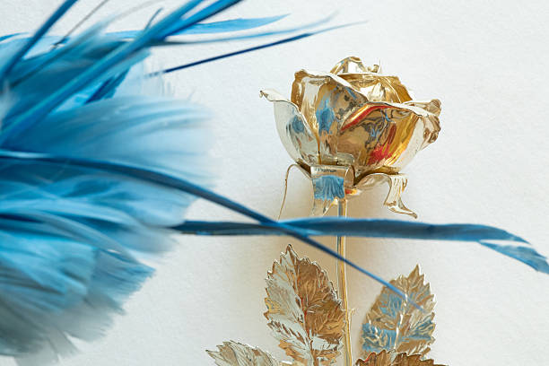 Golden metallic rose and light blue feathers on white background close-up and empty space