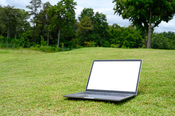 Laptop with blank screen placed on on fresh grass field. Technology lifestyle concepts.