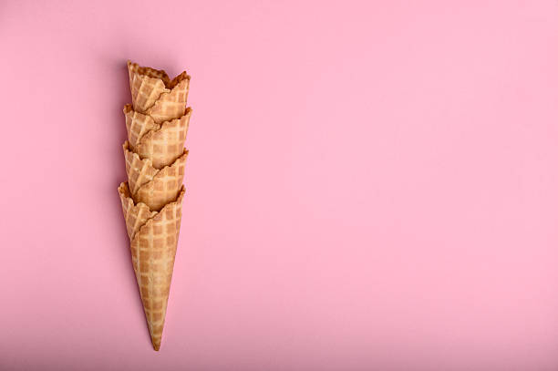 Four waffle cones are neatly stacked, showcasing their crisp texture against a bright pink background, perfect for holding ice cream
