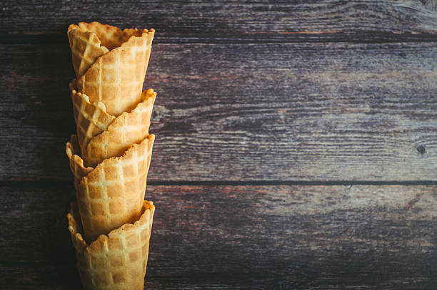 Several waffle cones are neatly stacked, prepared for delicious ice cream, set against a rustic wooden backdrop.
