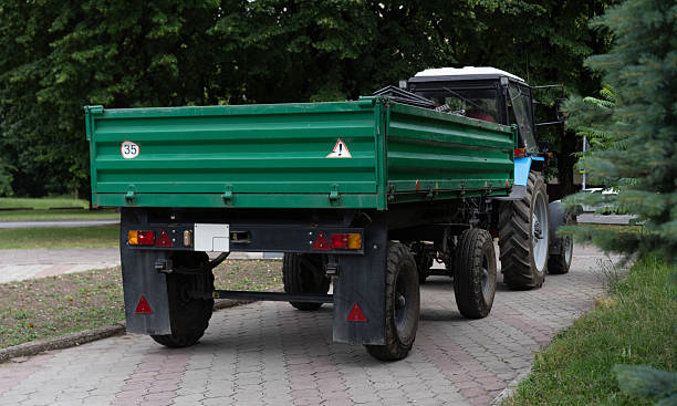 istock Green tractor with a trailer parked on a paved pathway surrounded by trees in a rural area during daylight hours 2222848015