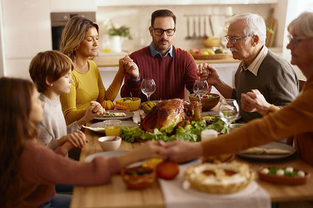 istock Religious extended family saying grace before Thanksgiving lunch. 2222856060