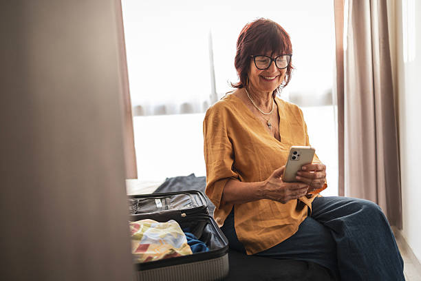 Woman packing suitcase and using smartphone in modern bright bedroom