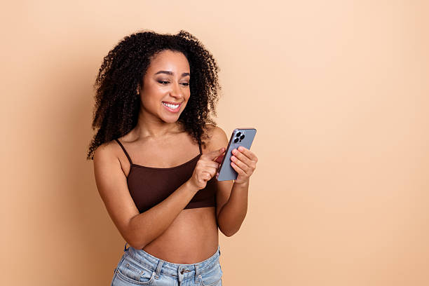 istock Confident young woman using smartphone while enjoying leisure time against beige background in casual and stylish attire 2222864558