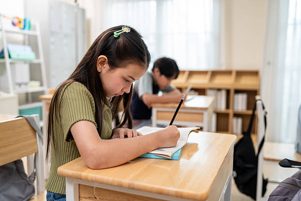 istock Asian student learning with teacher in classroom at elementary school. Adorable young schoolchildren sitting on the table, writing on book while tutor educate, teaching and explain the lesson in class 2222866997