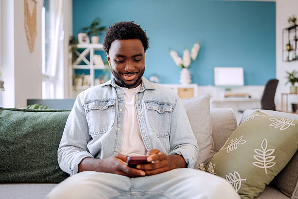 istock Casually clothed young man using smart phone while relaxing on a sofa at home 2222869318