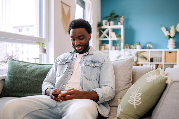 istock Casually clothed young man using smart phone while relaxing on a sofa at home 2222869325