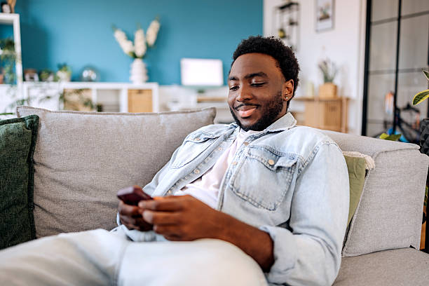 istock Casually clothed young man using smart phone while relaxing on a sofa at home 2222869332