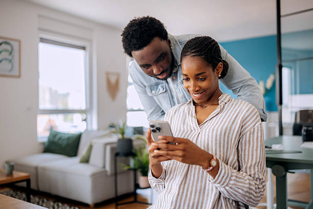 istock Young woman using smartphone at home with boyfriend looking over her shoulder 2222869362