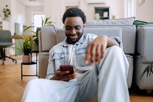 istock Casually clothed young man using smart phone while relaxing on a floor at home 2222869493