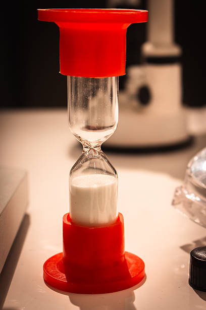 Small red hourglass with white sand on table. Sandglass on laboratory table. Time passing concept. Time measure equipment. Vintage clock. Retro timer.