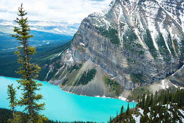 Snowy cliffs above a turquoise lake with a scree slope and green forest