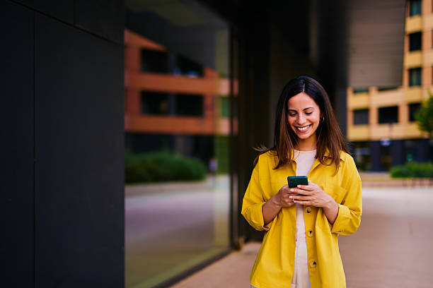 istock Woman Outdoors Smiling While Looking at Smartphone in an Urban Setting 2222874846