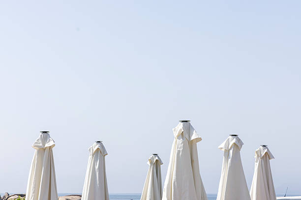 A row of white umbrellas are lined up on the beach. The umbrellas are open and facing the ocean. The scene is peaceful and serene, with the umbrellas providing a sense of shelter and relaxation
