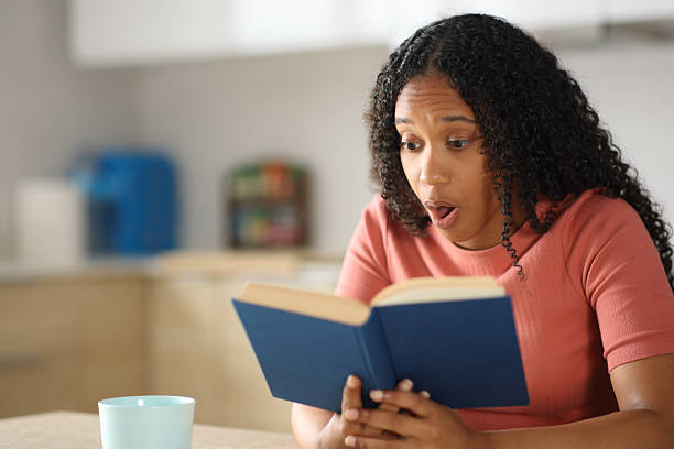 istock Amazed black woman reading a paper book in a kitchen 2222878990