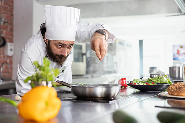 istock Head chef in restaurant kitchen adds a final touch of herbs to plated dish 2222879860