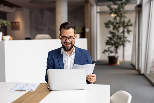 istock Happy businessman working on laptop and reading documents in modern office 2222881135