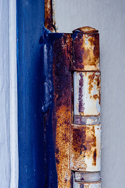 Close-up of a rusty hinge, exhibiting significant deterioration and corrosion, attached to a vibrant blue door, highlighting the effects of weathering and time