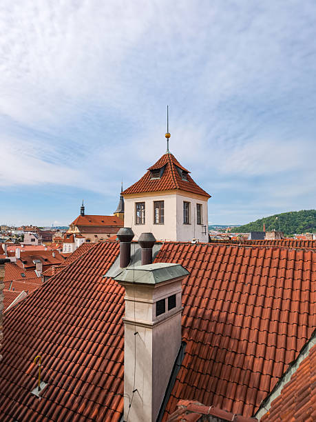 White tower emerging from prague's red roofs under cloudy sky