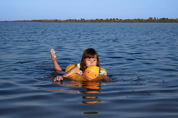 A child paddles gently in a serene lake while wearing a floatation device.