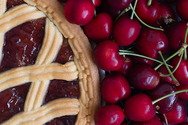 Close-up view of a cherry pie next to fresh red cherries on a table.