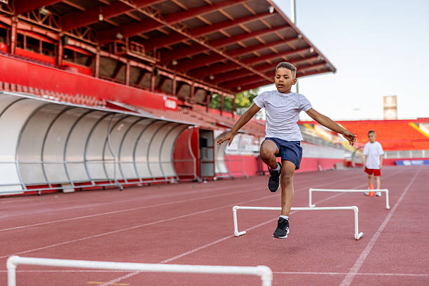 A female collegiate heptathlete jumps hurdles during a one-on-one training session with her coach.