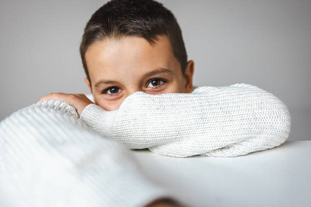 A young child posing happily, leaning on their arms while wearing a cozy white sweater.