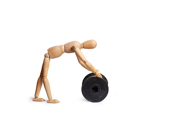 A wooden toy mannequin pushing a thread spool on white background