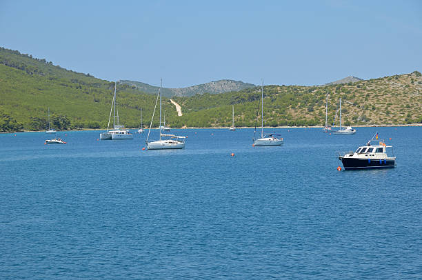 Kornati Islands bay, calm crystal clear water with boats against blue sky.