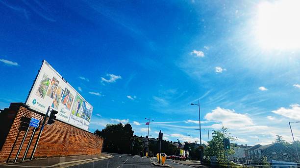Portadown, Northern Ireland - June 22, 2025. A road intersection with a brick wall on the left displaying a large Translink advertisement. Traffic lights, road signs, and a few cars are visible, with greenery and buildings in the background.