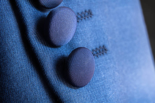 Close-up photograph showing dark blue fabric buttons sewn onto a similarly toned textile, emphasizing stitching detail, form, and craftsmanship