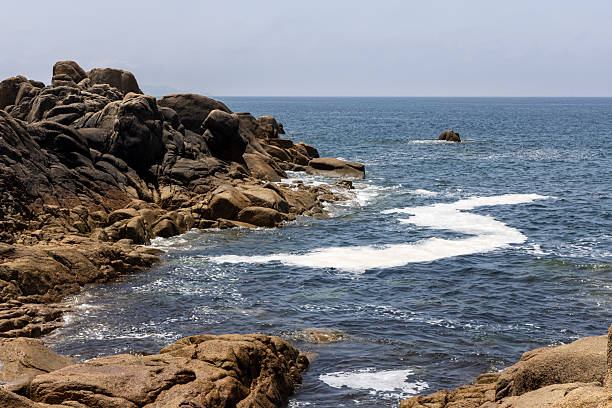 The ocean is calm and the sky is clear. The rocks are scattered along the shoreline, creating a beautiful and serene scene