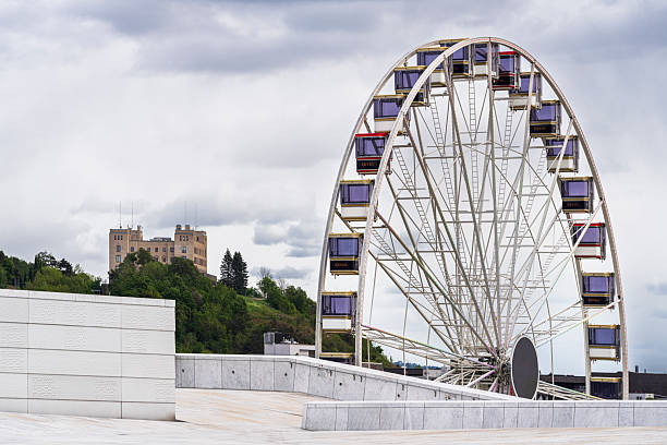 Aerial view of a Ferris wheel by a river in a cityscape at sunset, showcasing urban architecture and waterfront.