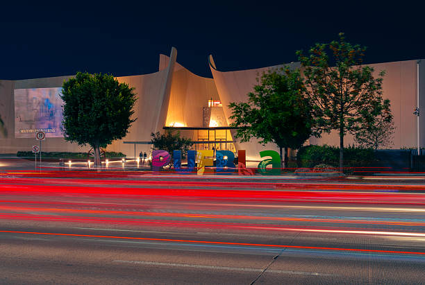 Puebla, Pue., Mexico - March 27, 2021: shot in the evening with rays from passing cars on the walls of entrance Museo Internacional del Barroco in the evening. the walls are illuminated with yellow lamps. the sky is dark - the road is concrete, the walls are made of tiles.