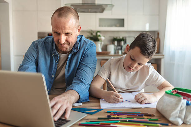 istock Father and son sitting side by side at home to work and study. Caucasian ethnicity father and son working and learning at home during the day. 2222907911