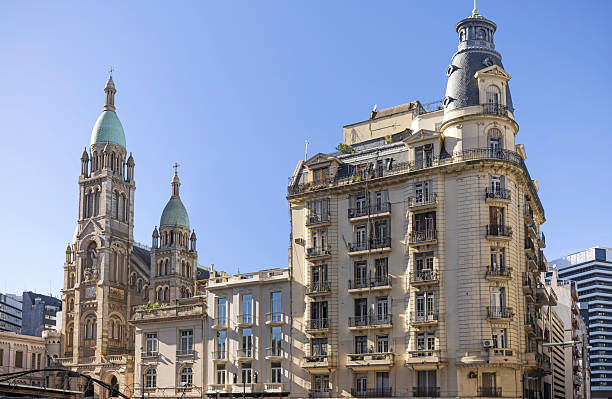 A woman holding a child's hand walks across a stone-paved square with vibrant decorations, surrounded by scenic buildings and natural landscapes under clear skies.