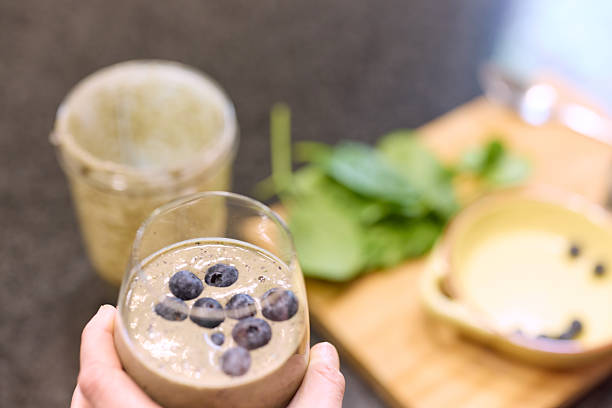A woman prepares a nutritious blueberry smoothie, surrounded by spinach and other fresh ingredients. The scene evokes a commitment to a balanced diet and emphasizes creating healthful, homemade beverages.