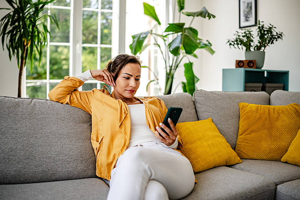 istock Engaged woman relaxing on a couch while using a smartphone in a bright living room 2222914832