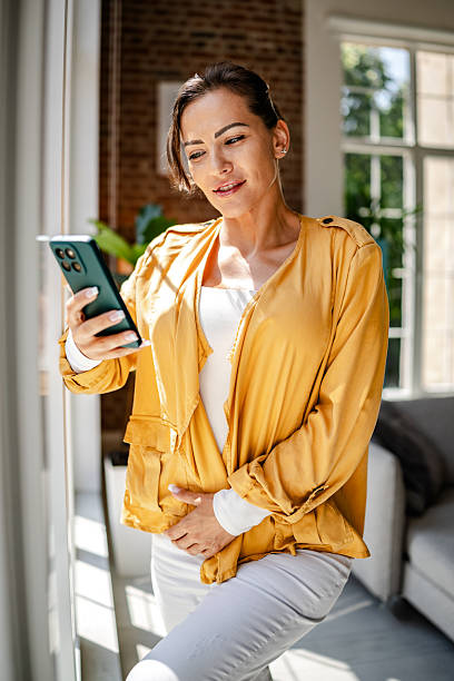 istock Woman using smartphone in a bright, modern living room with sunlight streaming through large windows 2222921490